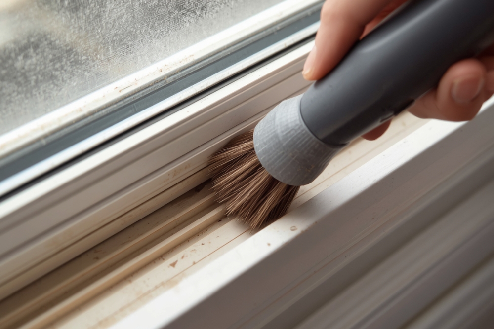 Un primer plano de una persona limpiando con un cepillo una ventana de aluminio blanco